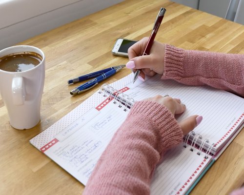 person writing in an agenda book on a wooden desk